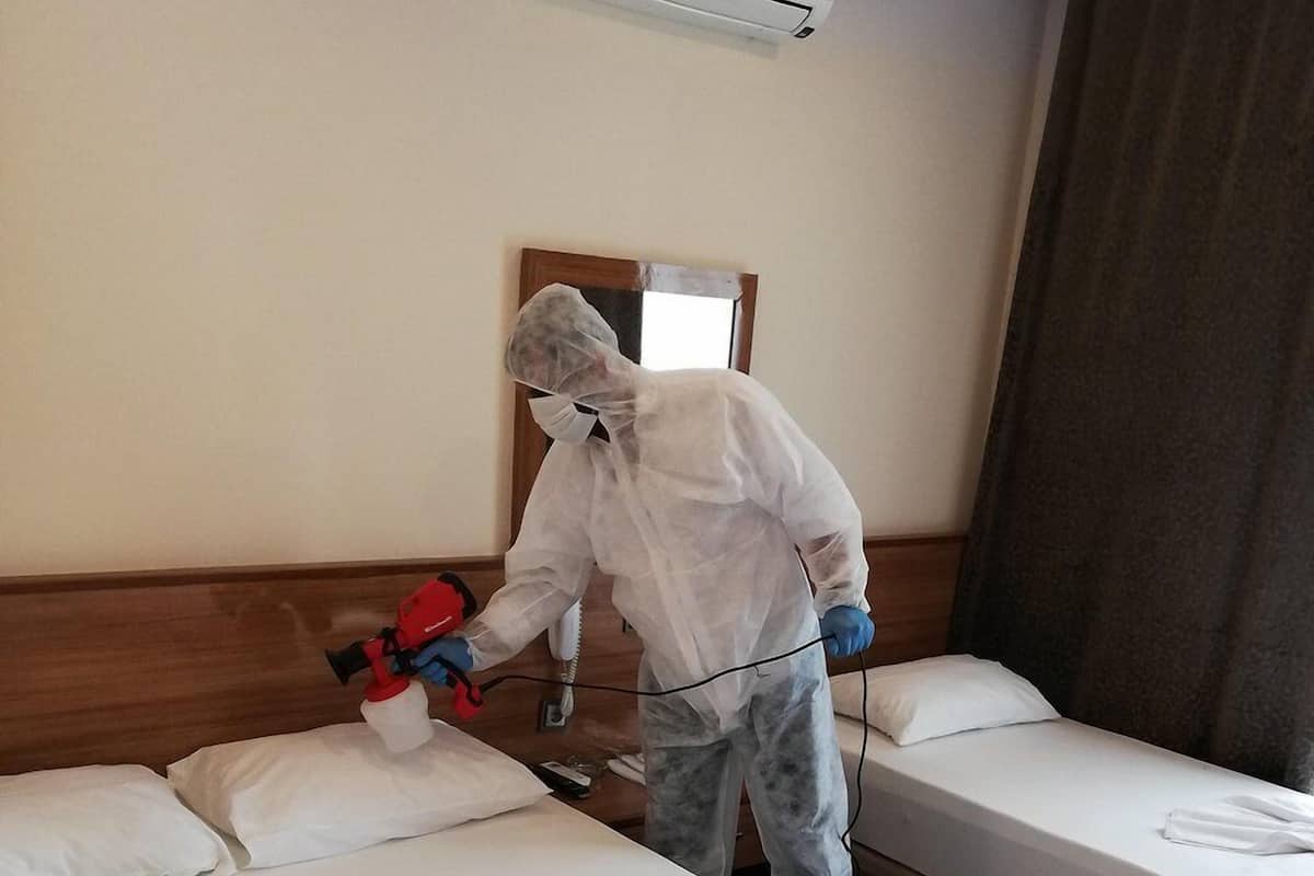 En person i skyddskläder städar ett hotellrum med en dammsugare.