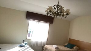 Een hotelkamer met twee bedden, een kroonluchter, een raam met gordijnen en een radiator.