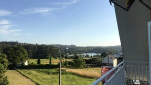 Een balkon met uitzicht op een landelijk landschap, met velden, bomen en een verre waterpartij.