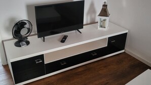 A white entertainment unit with a flat-screen TV, a remote control, and a decorative lantern. - Apartment cozy in the DG (Alzey)