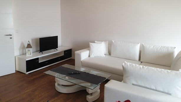 A modern living room with a white sofa, a glass coffee table, and a TV on a white console. - Apartment cozy in the DG (Alzey)