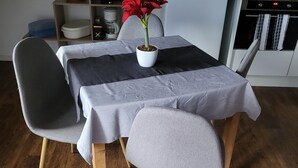 A dining area with a table covered by a grey tablecloth, two grey chairs, and a potted red plant. - Apartment cozy in the DG (Alzey)