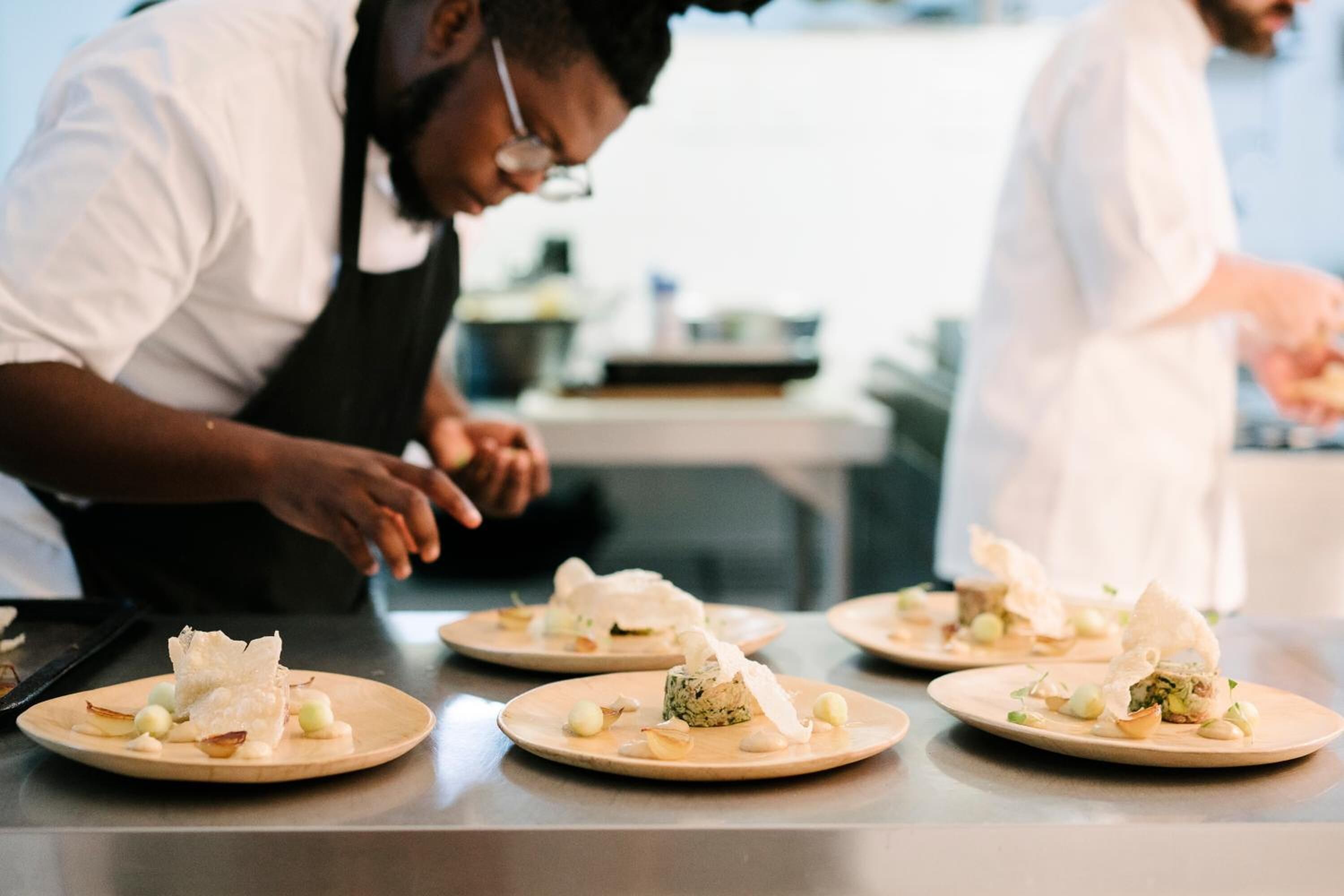 Chefs preparing dishes on plates in a kitchen setting.