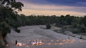 Paisaje desértico con una mesa dispuesta para una comida, rodeada de velas.