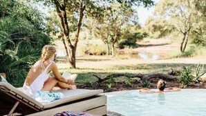 Una persona sentada en una terraza de madera junto a una piscina, leyendo un libro.