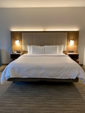 A hotel room with a large bed, two bedside tables, and wall-mounted lamps.