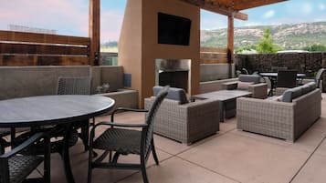 Un área de patio al aire libre con una mesa redonda, mobiliario de mimbre, un muro de piedra y vistas a un paisaje montañoso.