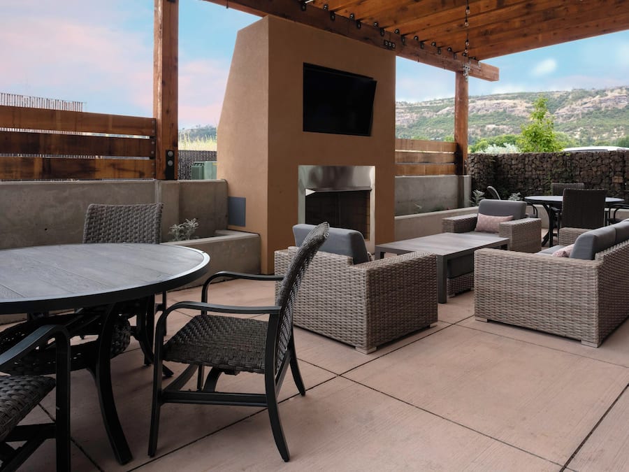 An outdoor patio area with a round table, wicker furniture, a stone wall, and a view of a mountainous landscape.