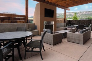 Un espace extérieur aménagé en terrasse, avec une table ronde, des meubles en osier, un mur en pierre et une vue sur un paysage montagneux.