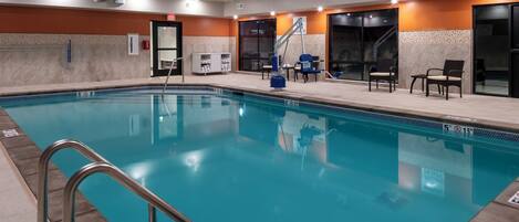 A swimming pool with a no diving sign, lounge chairs, and a tiled wall.