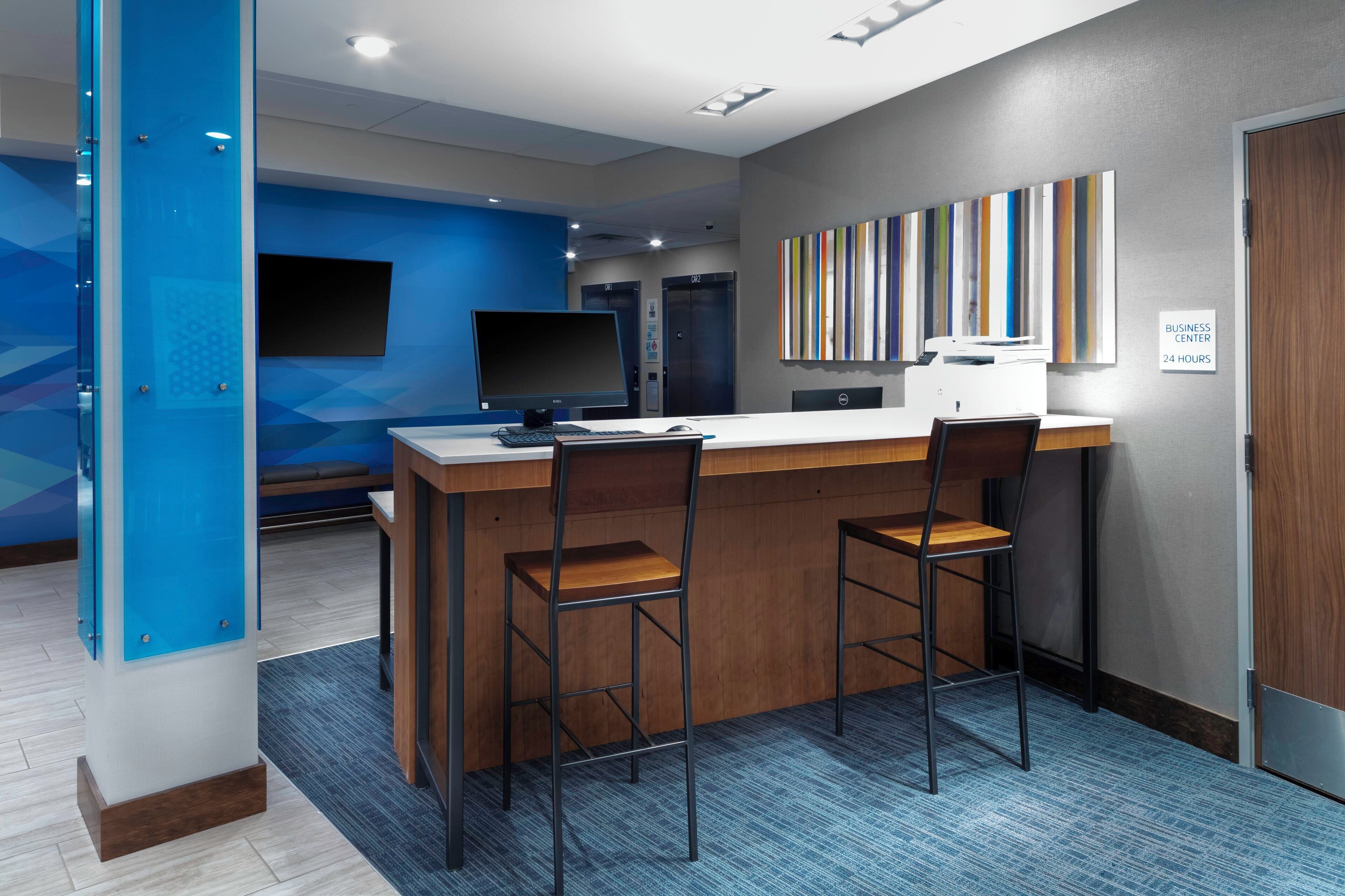 A modern office space with a reception desk, two bar stools, a flat-screen monitor, a desktop computer, and a printer.