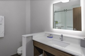 A modern bathroom with a white sink, a mirror, and a shower area.