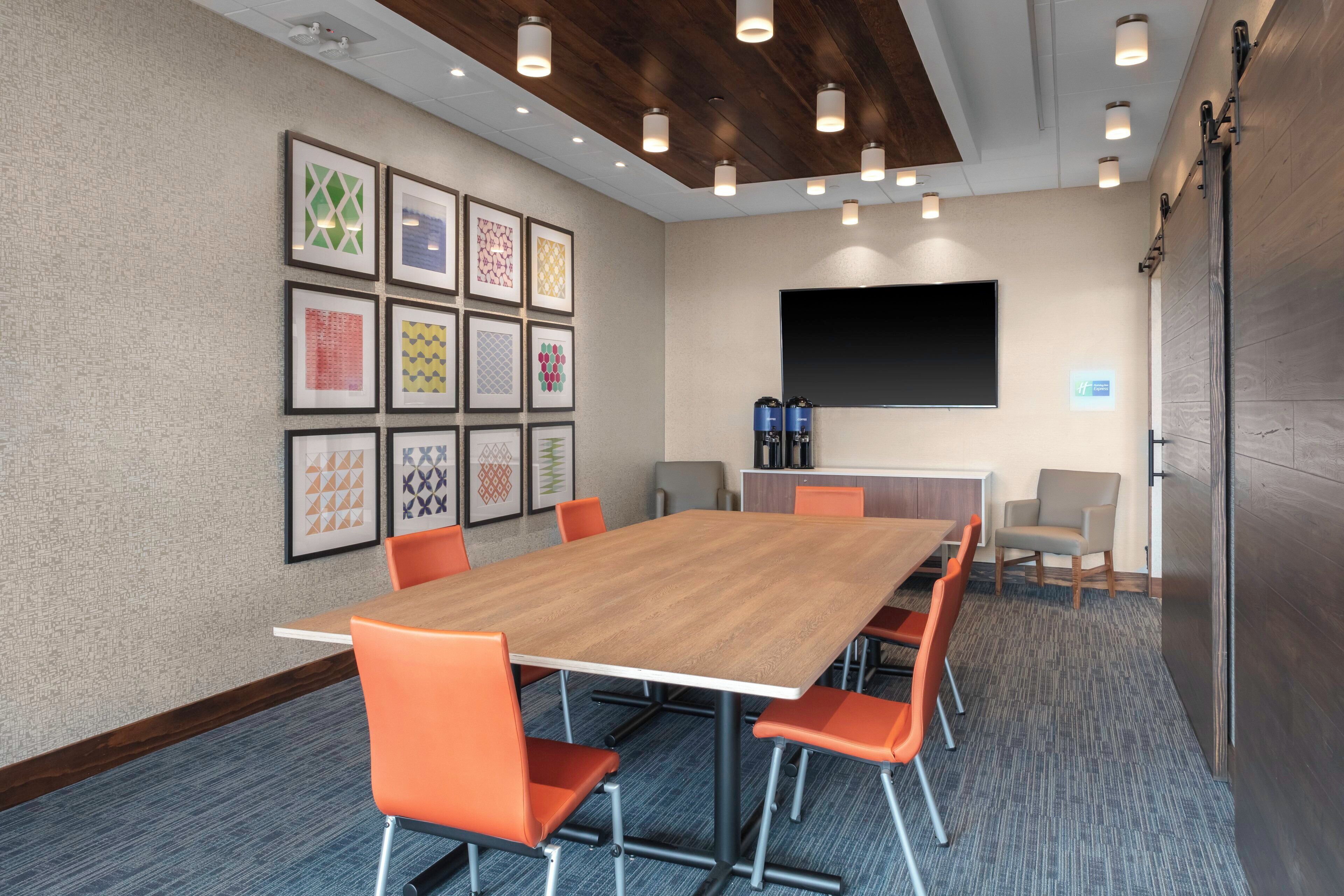 A conference room with a long table, orange chairs, a flat-screen TV, and framed artwork on the wall.