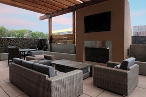 An outdoor patio area with wicker furniture, a flat-screen TV mounted on a wall, and a stone wall in the background. - Holiday Inn Express & Suites The Dalles by IHG (The Dalles)
