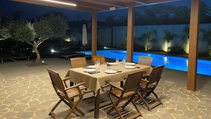 An outdoor dining area with a pool, wooden chairs, and a table set for four. - Signorino Suites&Pool (Marsala)