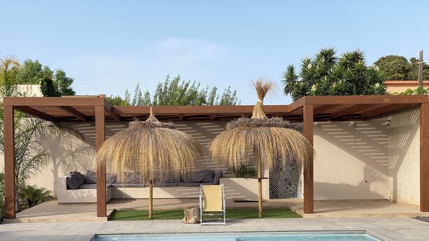 A swimming pool with a pergola and seating area, surrounded by greenery and a clear sky. - Signorino Suites&Pool (Marsala)