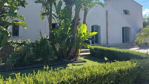 A white building with arched windows and a well-maintained garden with various plants. - Signorino Suites&Pool (Marsala)