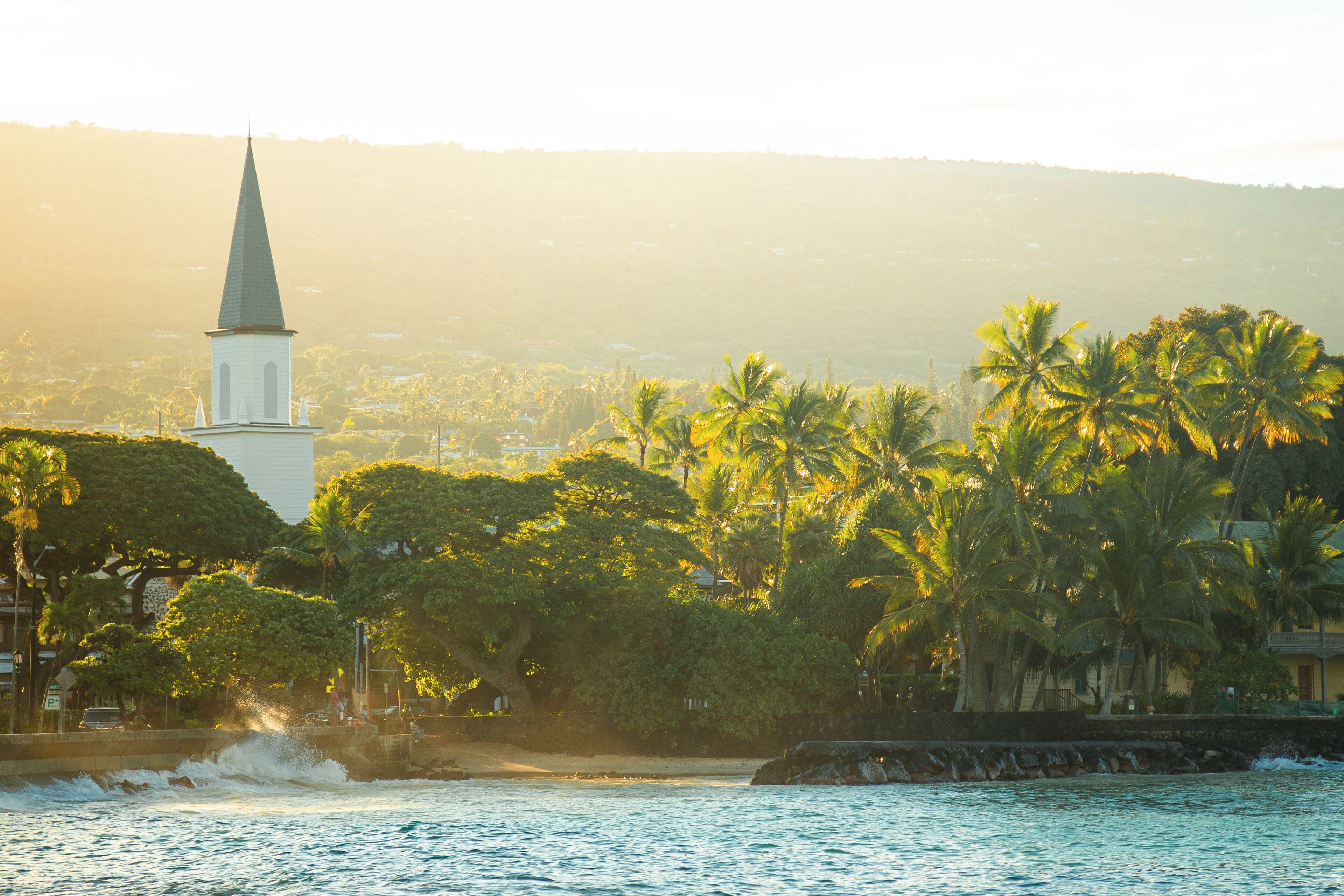 A coastal scene with a church spire, palm trees, and a rocky shoreline.