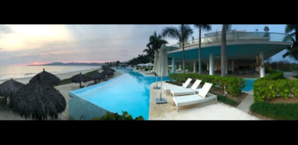 Relax by the serene pool surrounded by thatched umbrellas and lounge chairs.