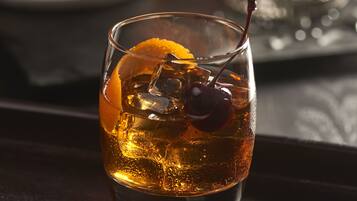 Un vaso de bebida color ámbar con hielo y una cereza, sobre una superficie de madera oscura.