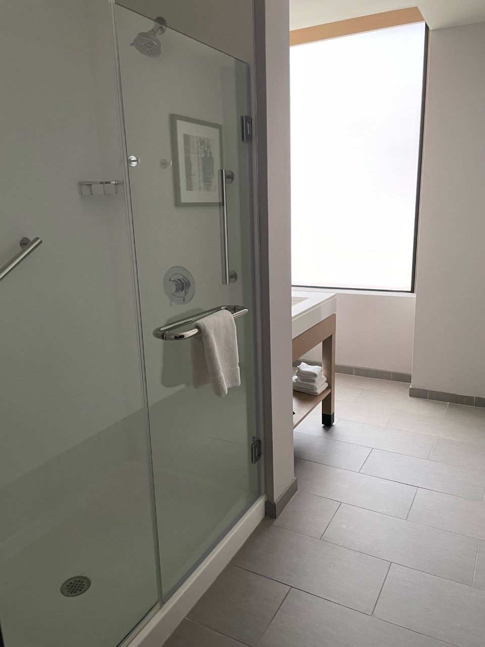 A modern bathroom with a glass shower enclosure, a white sink, and a window providing natural light.