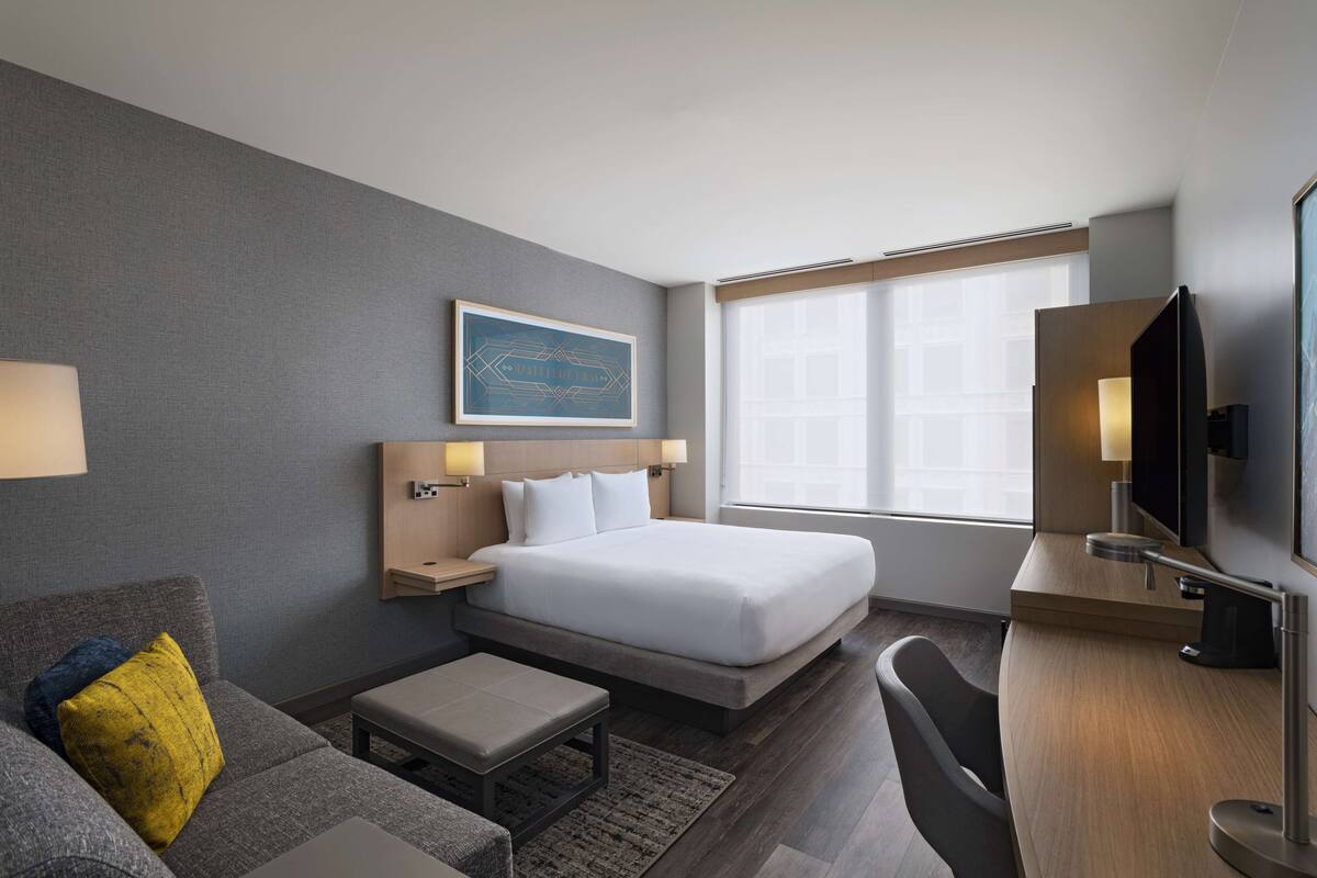 Ein modernes Hotelzimmer mit einem großen Bett, einem Schreibtisch, einem Stuhl, einer Couch und einem Fernseher.