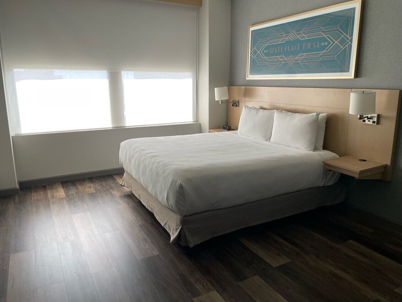 Ein Hotelzimmer mit einem großen Bett, einem Nachttisch, einer Wandleuchte und einem Fenster mit Jalousien.
