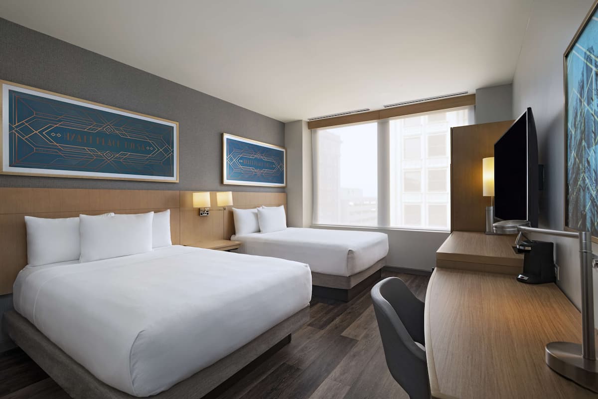 Ein Hotelzimmer mit zwei Betten, einem Schreibtisch, einem Fernseher und Bildern an den Wänden.