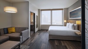 A modern hotel room with a bed, a sofa, and a desk. There is a large window with a view of the city. - Hyatt Place Tulsa Downtown (Tulsa)