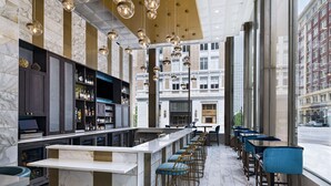 A modern bar area with marble flooring, a central bar counter, and blue bar stools. - Hyatt Place Tulsa Downtown (Tulsa)