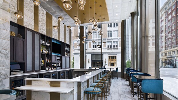 A modern bar area with marble flooring, a central bar counter, and blue bar stools. - Hyatt Place Tulsa Downtown (Tulsa)