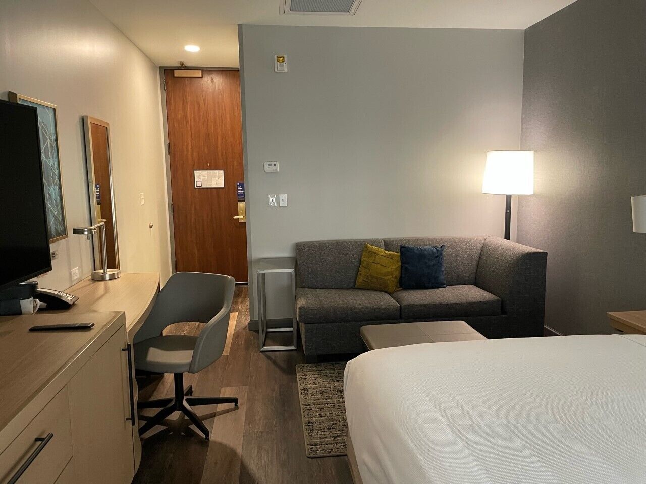 A hotel room with a desk, chair, sofa, and bed.