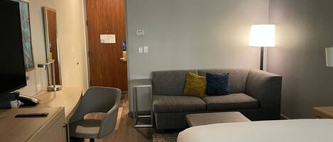 A hotel room with a desk, chair, sofa, and bed.