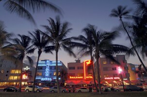 Un hotel con letrero de neón, palmeras y coches estacionados.