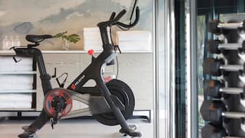 A stationary bike in a room with a wooden floor, a towel rack, and a wall with a painting.