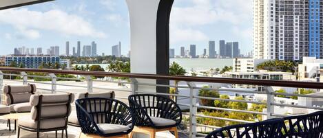 A terrace with outdoor seating, a view of a city skyline, and a body of water.