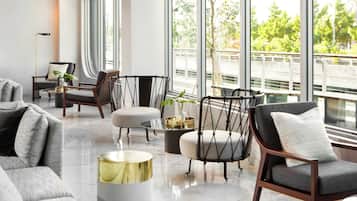 Una sala moderna con sofá, sillones, una mesita de centro y vistas a un puente y vegetación al exterior.