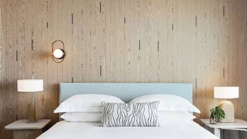 A hotel room with a wooden wall, a bed with white bedding, two bedside tables with lamps, and a single decorative pillow.