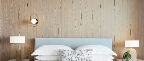 A hotel room with a wooden wall, a bed with white bedding, two bedside tables with lamps, and a single decorative pillow.