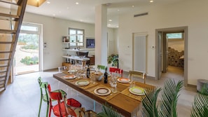 Un espace de repas moderne, avec une longue table dressée pour un repas, entourée de chaises, et donnant sur le jardin.