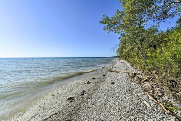 Een kiezelstrand met helder water en bomen aan de rechterkant.
