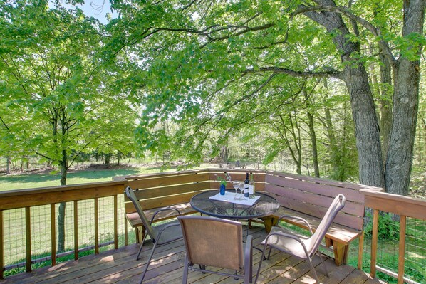 A wooden deck with a round table and chairs, surrounded by trees. - Updated Home w/ Deck: 2 Mi to Sister Bay Beach! (Sister Bay)