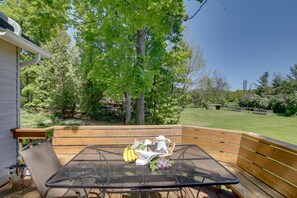 A patio with a table set for breakfast, surrounded by wooden deck and trees. - Updated Home w/ Deck: 2 Mi to Sister Bay Beach! (Sister Bay)