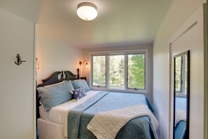 A bedroom with a large bed, a window with a view of trees, and a ceiling light. - Updated Home w/ Deck: 2 Mi to Sister Bay Beach! (Sister Bay)