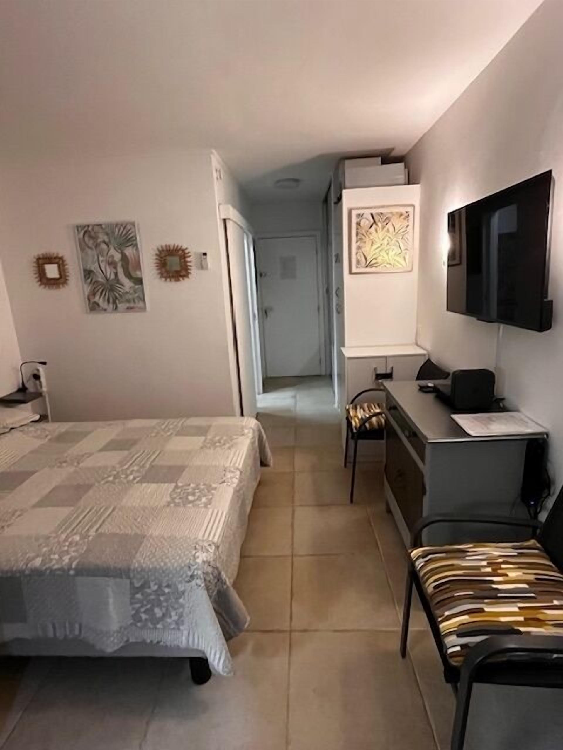 A bedroom with a bed, a desk, a chair, a TV, and artwork on the walls.