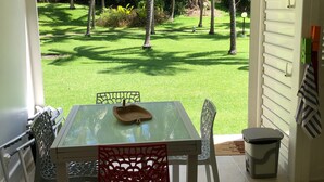 A patio with a glass table and chairs, a ceiling fan, and a view of a well-maintained lawn and trees. - Superb Studio "Lespiedsdansleau" Garden level, sea view 2 Adults and 1 Child (SAINT FRANCOIS)