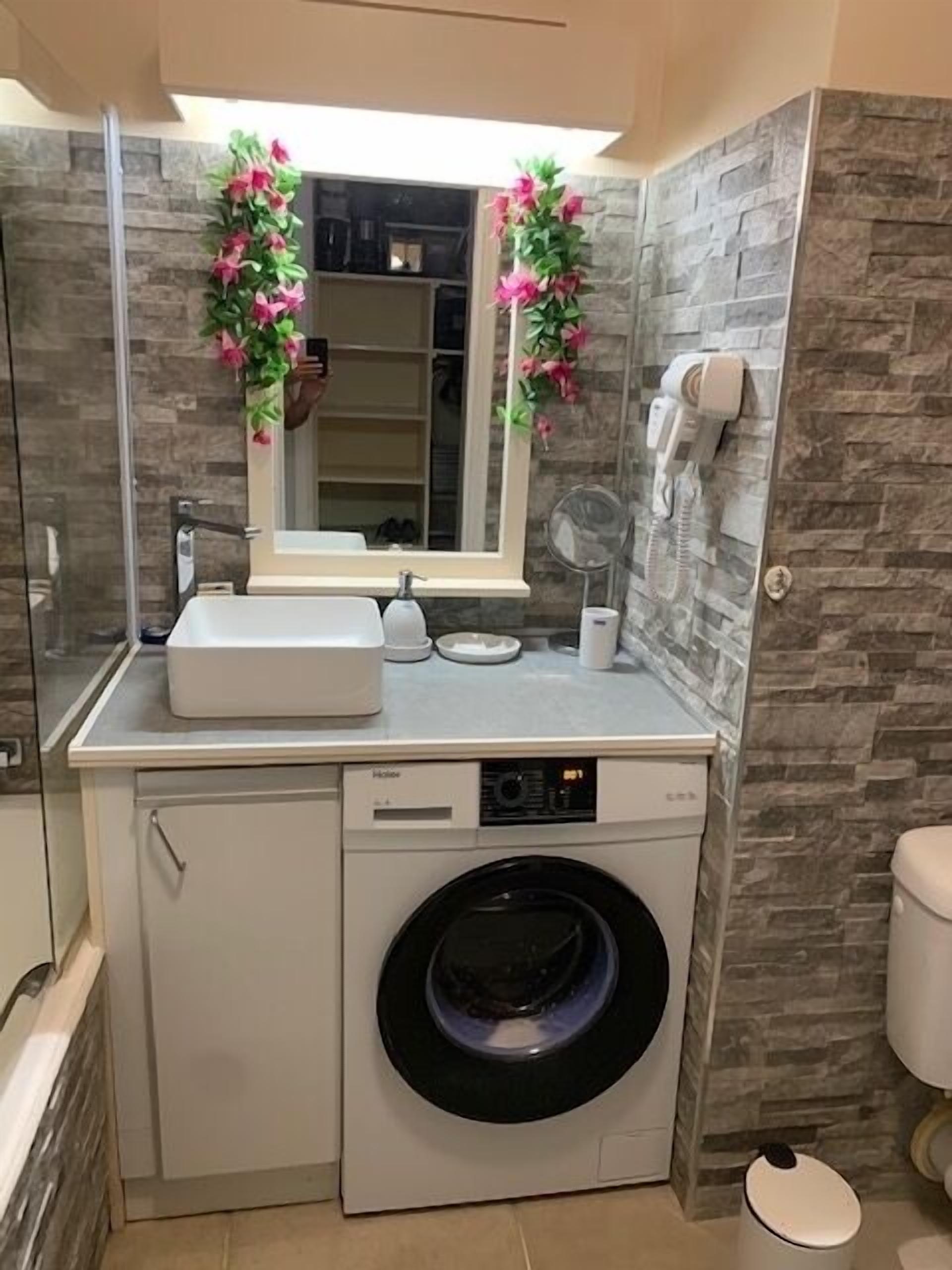 A compact bathroom with a washing machine, a sink, and a mirror.