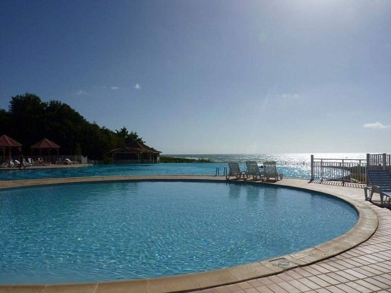 Una piscina amplia y transparente con sillones de descanso y vista al océano.