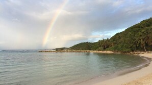 A beach with a rainbow, calm water, and a forested hill. - Superb Studio "Lespiedsdansleau" Garden level, sea view 2 Adults and 1 Child (SAINT FRANCOIS)