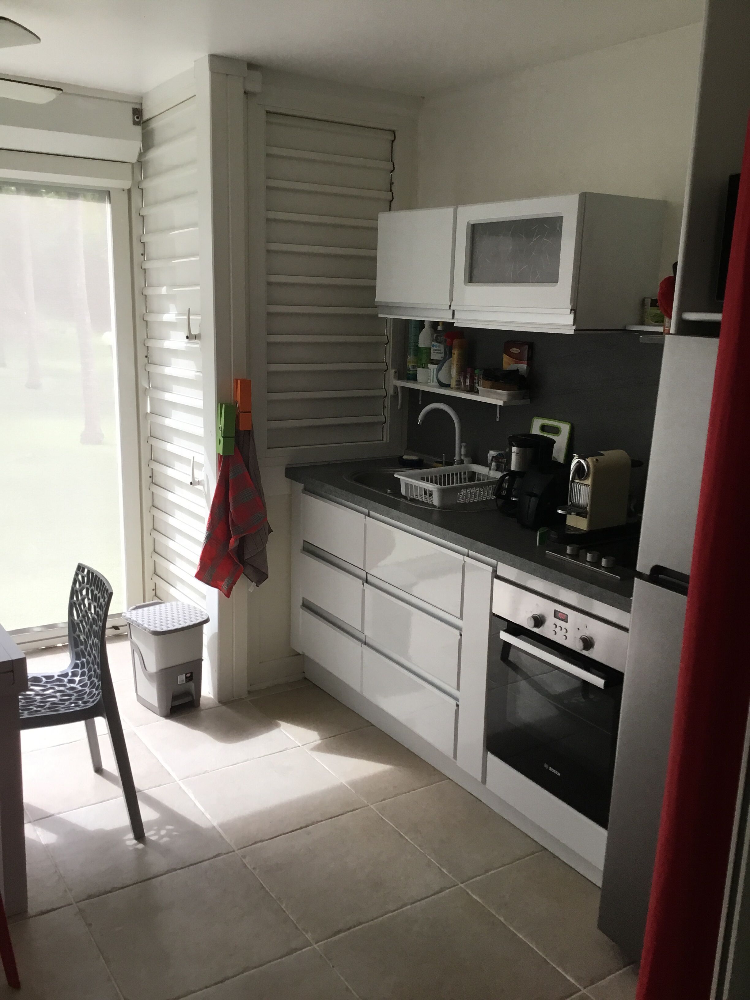 Eine kleine Küche mit weißen Schränken, einer eingebauten Mikrowelle, einem Spülbecken und einem Backofen von Bosch.